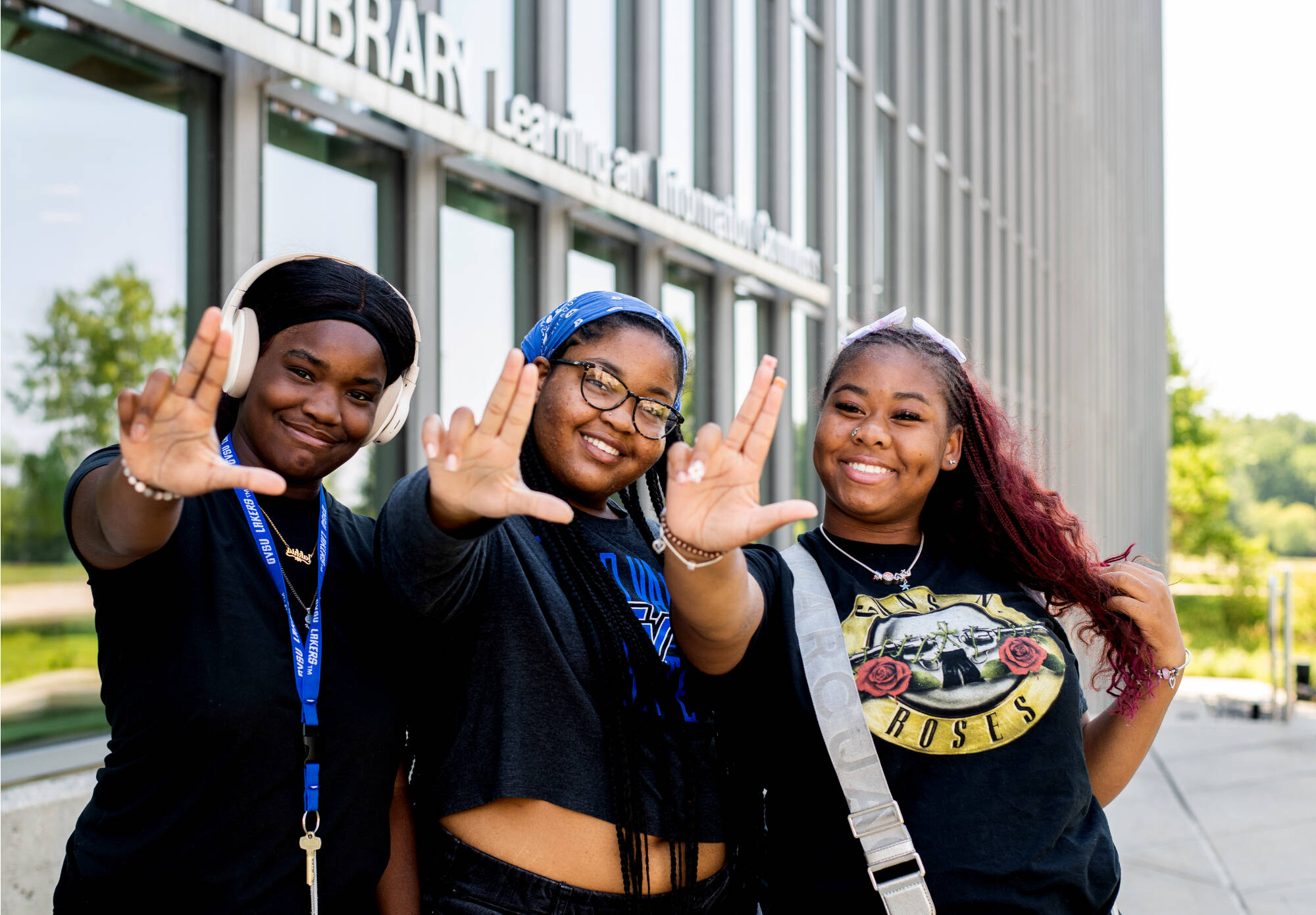Three students pose with Laker hands in front of the library